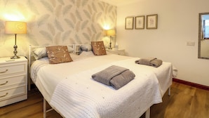A bedroom with a large bed, two bedside tables, a nightstand, a mirror, and a wall with feather-patterned wallpaper. - Kingfisher (Diss)