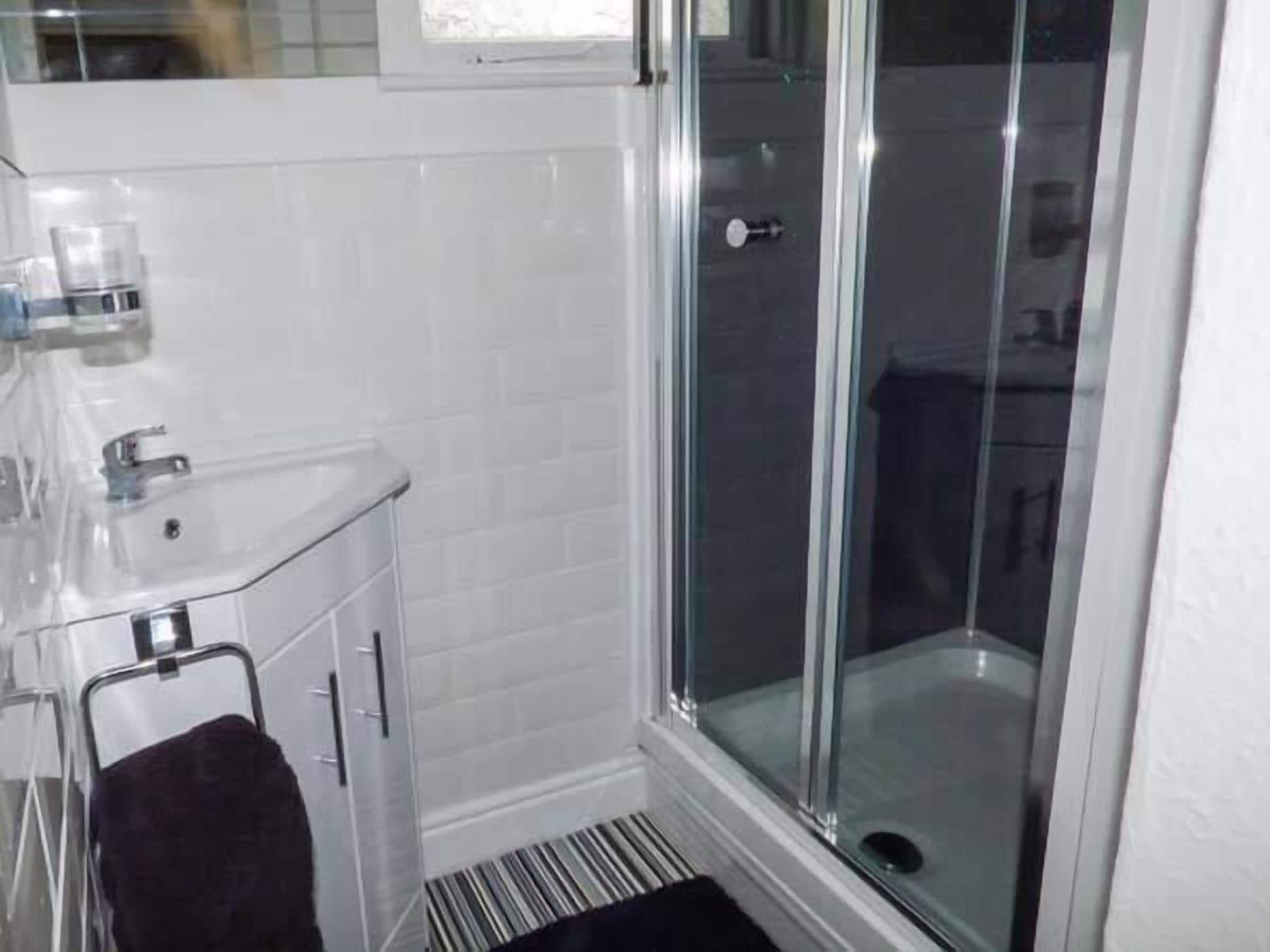 A bathroom with a glass shower enclosure, a white sink, and a towel rack.