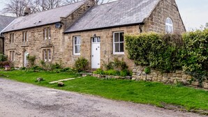 Une maison en pierre avec un toit en pente, une porte blanche et un petit jardin.