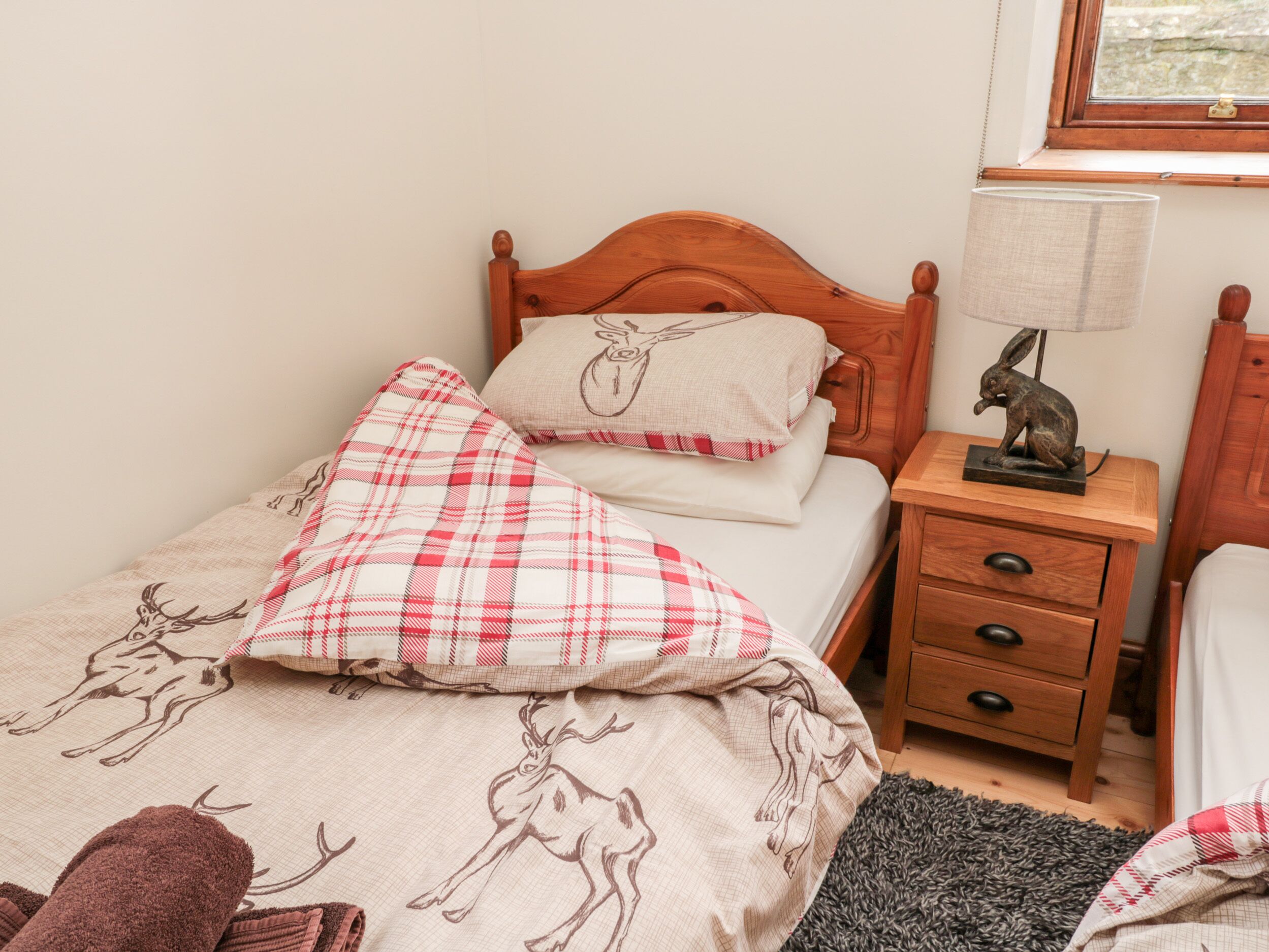 Una cama individual con cabecera de madera, una mesita de noche con lámpara y un cajón.