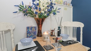 Et spisebord med blomsterdekoration, et skilt med teksten "Hello with Love", og et "Velkommen"-skilt over en hylde.