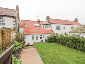 Traditional home with a well-maintained garden and red-tiled roof, featuring a paved pathway and outdoor seating area.