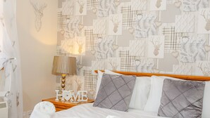 Una cama bien hecha con sábanas blancas y dos almohadas grises, una lámpara de noche y una pared decorada con diversos diseños y la palabra 'HOME'.