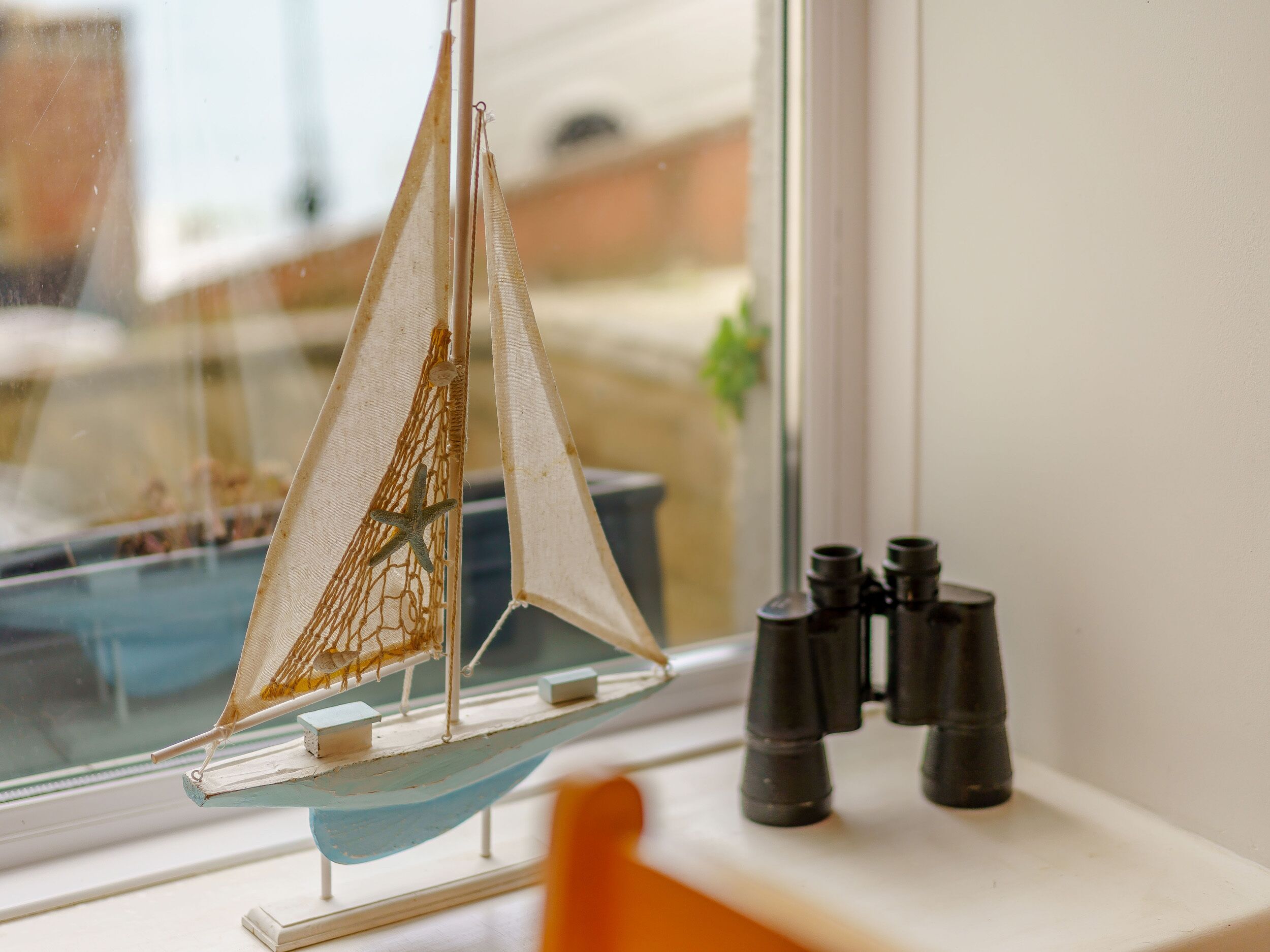 Un modellino di barca a vela su un davanzale con un binocolo accanto.