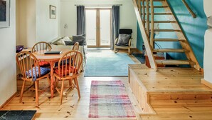 Una habitación acogedora con una mesa de madera, sillas, un sofá y una escalera que sube a un nivel superior.