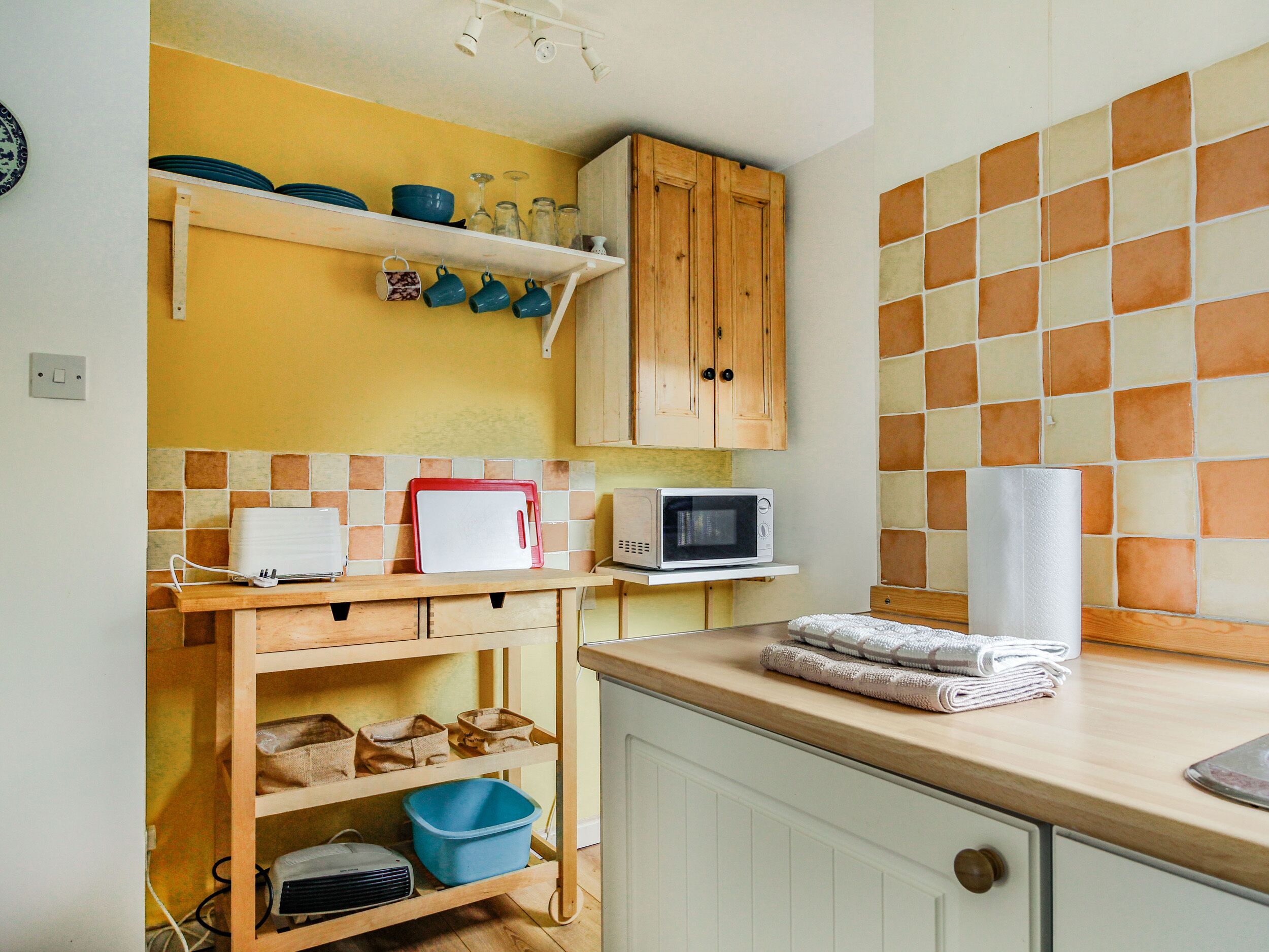 A kitchen with wooden cabinets, a microwave, and a shelf with dishes.
