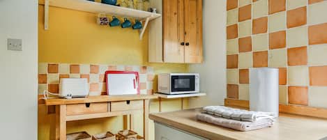A kitchen with wooden cabinets, a microwave, and a shelf with dishes.