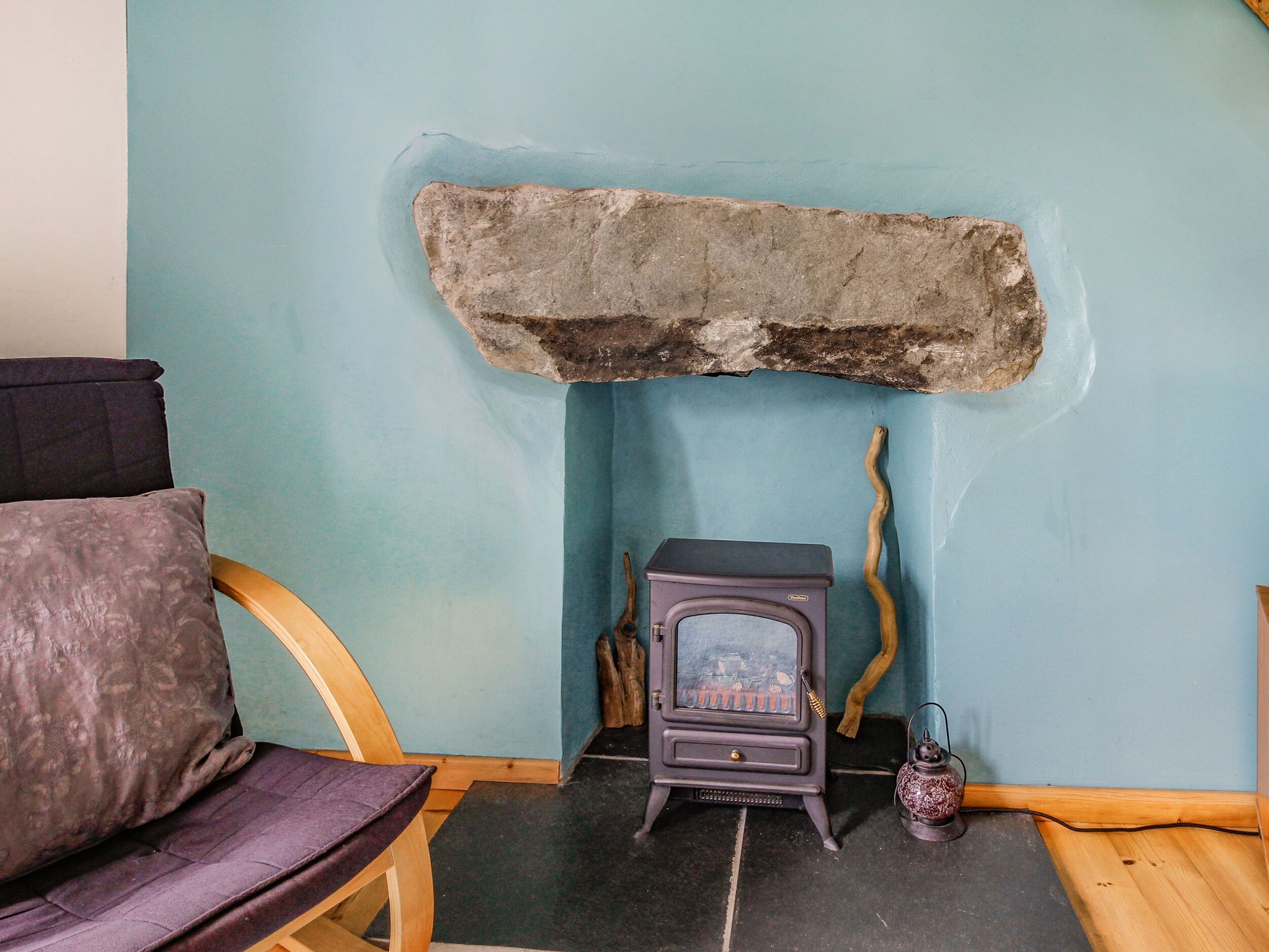 A room with a stone fireplace, a wooden chair, and a vintage stove.