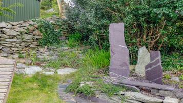 Un jardín con un muro de piedra, un banco de madera y dos grandes esculturas de piedra.