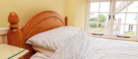 A bed with a wooden headboard, a bedside table, and a window with a view of buildings and greenery.