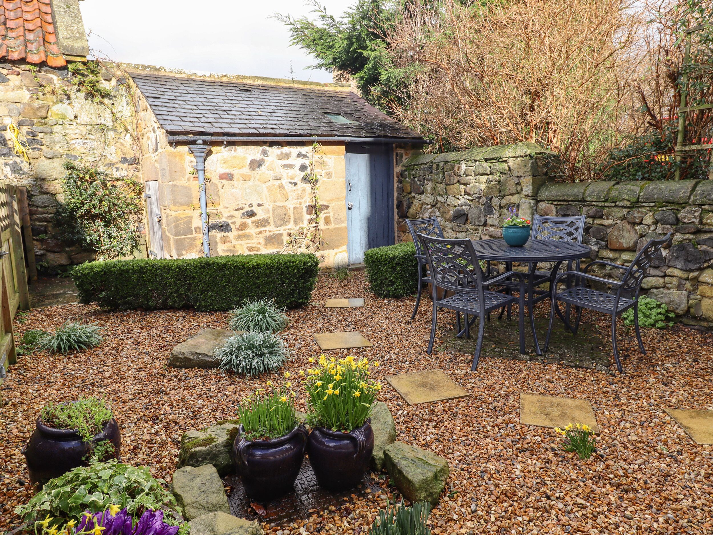 A stone building with a tiled roof, a small door, and a garden area with a table and chairs.