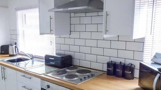 A modern kitchen with white cabinets, a wooden countertop, a gas stove, a kettle, a toaster, and black containers labeled 'TEA' and 'SUGAR'. - Flat 1 (Bridlington)
