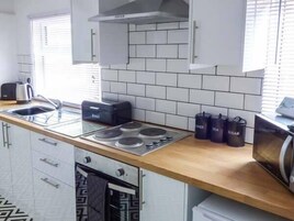 Cocina moderna con armarios blancos, encimera de madera, estufa a gas, hervidor, tostadora y recipientes negros etiquetados 'TÉ' y 'AZÚCAR'.