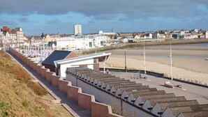 A coastal promenade with a series of steps leading down to the beach, a row of flags, and buildings in the background. - Flat 1 (Bridlington)