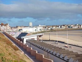 Un paseo marítimo con una serie de escalones que bajan a la playa, una hilera de banderas y edificios al fondo.