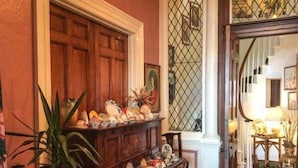 Een kamer met een houten piano, een bloempot en een decoratieve spiegel.