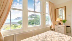 Een slaapkamer met een groot raam, een bed, een dressoir en een spiegel.
