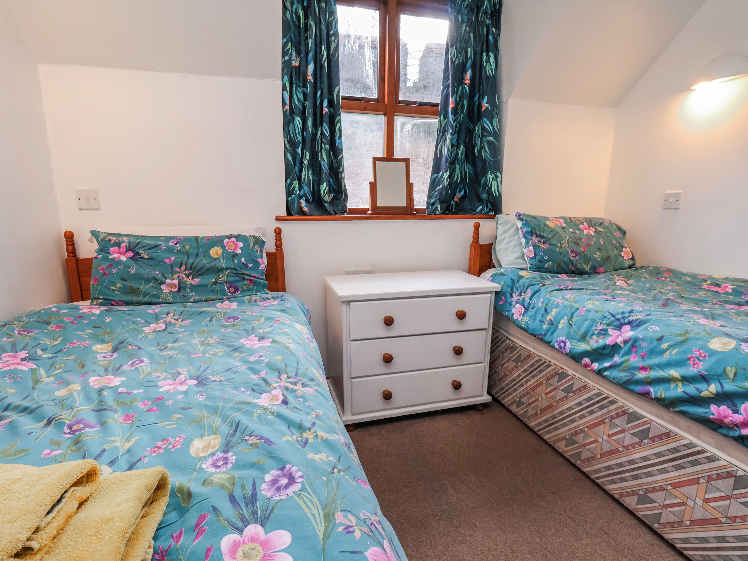 A bedroom with two single beds, a dresser, a window with curtains, and a mirror.