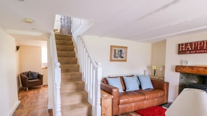 A staircase leading to a second floor, a brown leather sofa with blue cushions, a red rug, and a white lamp. - Bank House (Newcastle Emlyn)