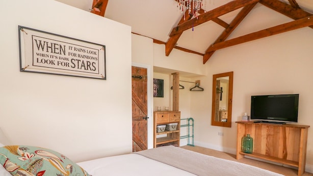 A bedroom with a bed, pillows, a wooden dresser, a television, and a mirror. - Bank House (Newcastle Emlyn)