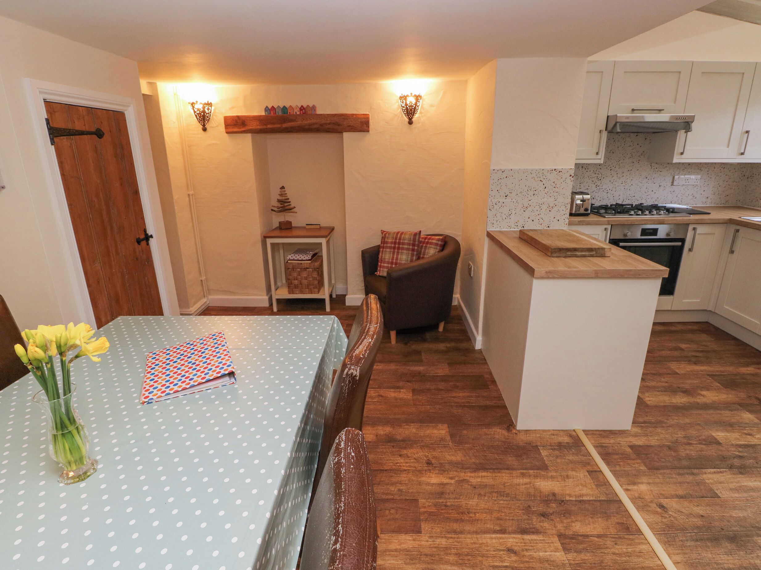 A compact kitchen with wooden flooring, a dining area with a table and chairs, and a small island with a countertop.