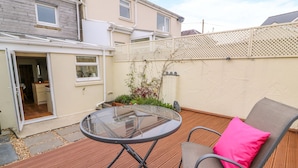 A patio with a glass table and two chairs, a wooden deck, and a house with a white fence and a garden. - Bank House (Newcastle Emlyn)