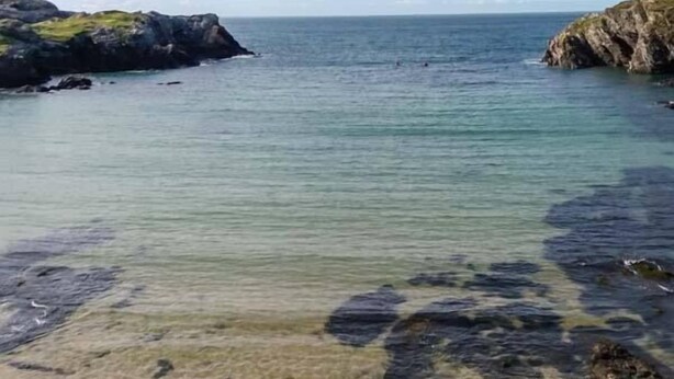 A coastal scene with clear water, rocky shores, and distant cliffs. - Llety'r Bugail (Maesteg)