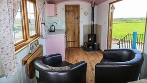 A cozy room with a wooden floor, a kitchenette, a fireplace, and two leather chairs. - Llety'r Bugail (Maesteg)
