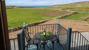 A patio with a table and chairs overlooking a grassy field and the sea. - Llety'r Bugail (Maesteg)