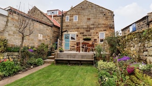 A stone building with a small garden, a wooden bench, and a blue door. - Mill Cottage (Saltburn-by-the-Sea)