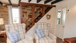 A room with two plaid armchairs, a wooden staircase, and a stone wall. - Mill Cottage (Saltburn-by-the-Sea)