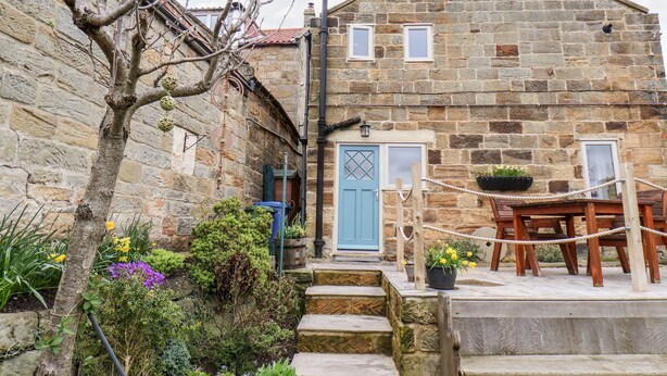 A stone building with a blue door, a wooden table, and potted plants. - Mill Cottage (Saltburn-by-the-Sea)