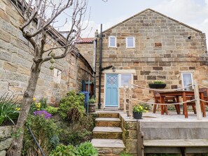 A stone building with a blue door, a wooden table, and potted plants. - Mill Cottage (Saltburn-by-the-Sea)