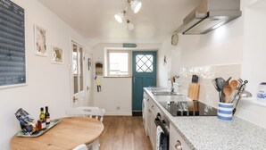 A kitchen with a wooden table, white chairs, a built-in oven, and a sink. - Mill Cottage (Saltburn-by-the-Sea)