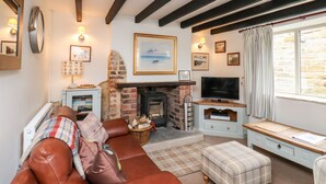 A cozy living room with a fireplace, a sofa, a television, and a window with curtains. - Mill Cottage (Saltburn-by-the-Sea)