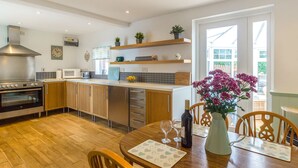 A modern kitchen with wooden cabinets, a stainless steel range hood, and a dining area with a wooden table and chairs. - Estuary View (Morpeth)