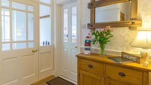 A hotel reception area with a wooden cabinet, a welcome sign, a vase with flowers, a lamp, and a mirror. - Estuary View (Morpeth)