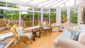 A conservatory with wicker furniture, a wooden table, and a view of a garden through large windows. - Estuary View (Morpeth)