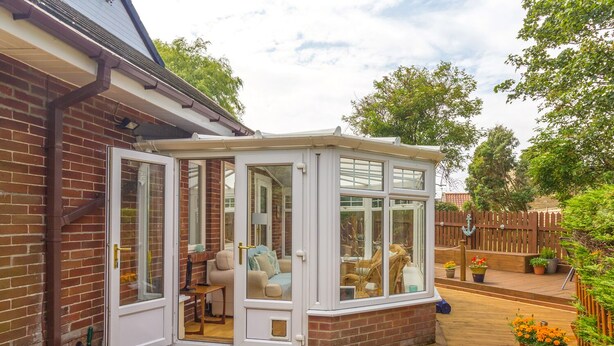 A conservatory with a brick exterior, a wooden deck, and a garden with potted plants. - Estuary View (Morpeth)