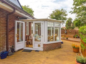 A conservatory with a brick exterior, a wooden deck, and a garden with potted plants. - Estuary View (Morpeth)