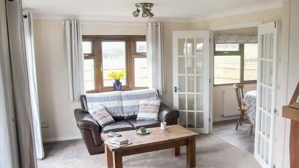 A cozy living room with a leather sofa, a wooden coffee table, and a view through a glass door. - The Dovecote (Bideford)