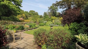 A garden with a stone pathway, a wooden bench, and various plants. - Kestrel Cottage (Grange-over-Sands)