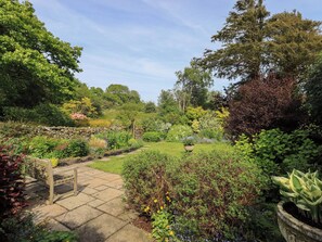 A garden with a stone pathway, a wooden bench, and various plants. - Kestrel Cottage (Grange-over-Sands)