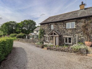 A stone house with a gravel driveway, a conservatory, and a garden with various plants. - Kestrel Cottage (Grange-over-Sands)