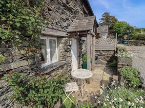 A stone house with a wooden door, a white-framed window, and a white outdoor table. - Kestrel Cottage (Grange-over-Sands)