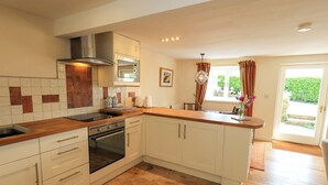 A kitchen with white cabinets, a stainless steel range hood, a built-in oven, and a wooden countertop. - Kestrel Cottage (Grange-over-Sands)