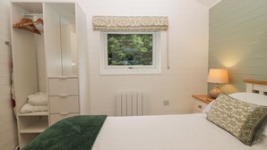 Une chambre à coucher avec un lit, une table de chevet avec une lampe, une fenêtre donnant sur des arbres, une armoire et un radiateur.