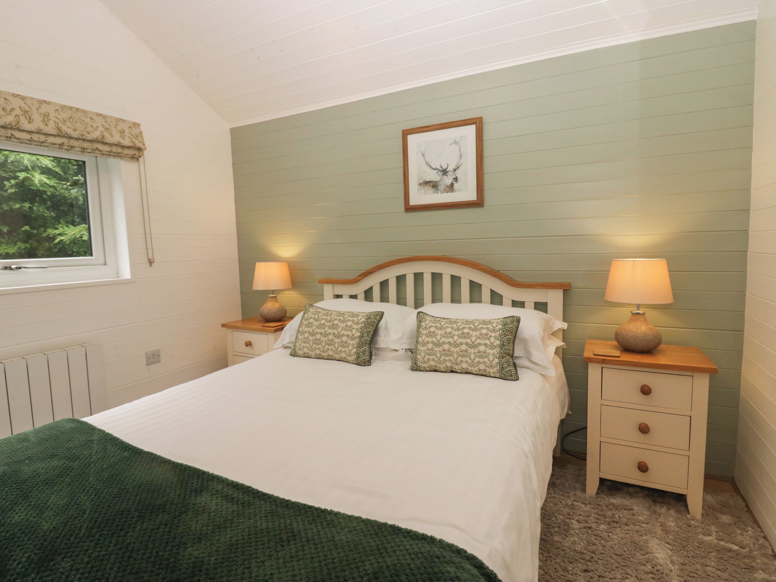 A bedroom with a bed, two bedside tables, a window, and a framed picture on the wall.