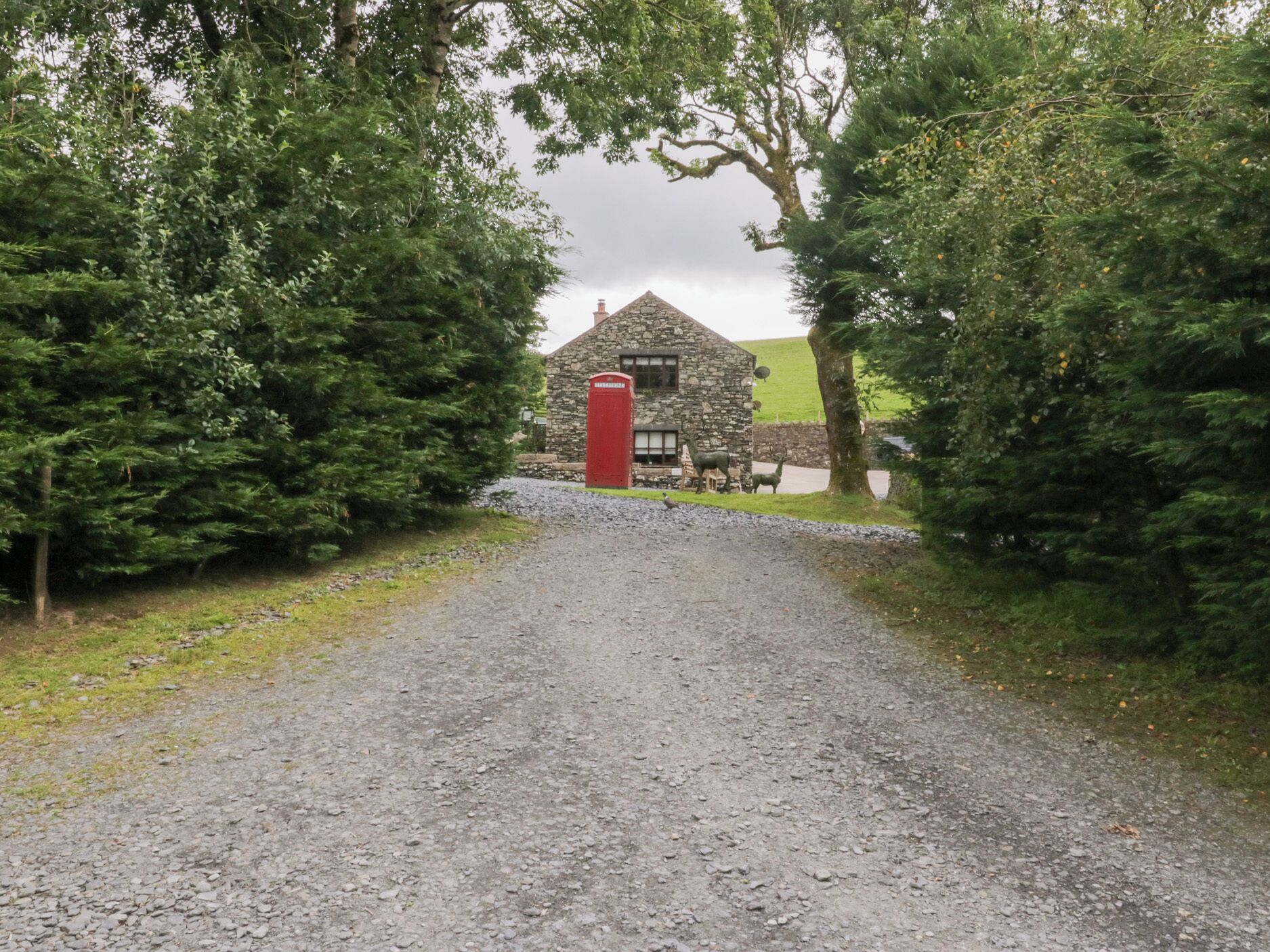 Un edificio de piedra con un buzón rojo, rodeado de árboles frondosos y un camino de grava que lo conduce.