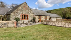A stone house with a sloped roof, a wooden bench, and a small garden area. - The Old Dairy (Newport)